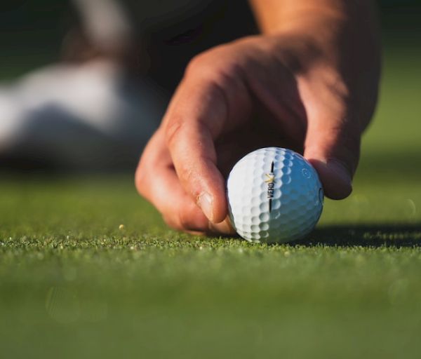 A person is placing a golf ball on the grass, likely preparing for a putt on a golf course.