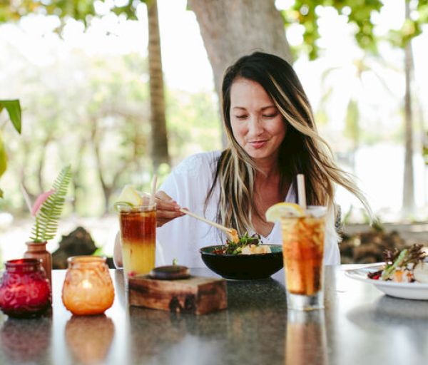 A person is sitting at an outdoor table, enjoying a meal with drinks and colorful candles, surrounded by nature.