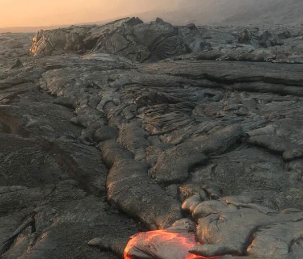 The image shows a landscape with solidified volcanic lava, featuring a small area of glowing molten lava in the foreground.