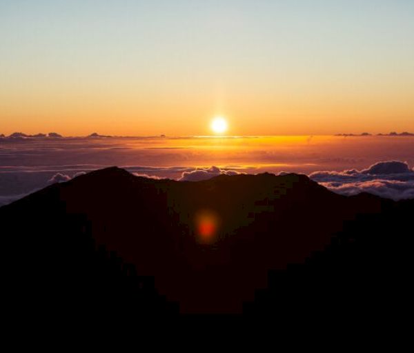 A stunning sunrise over a mountainous landscape, with the sun casting a golden glow over the horizon and clouds in the sky.